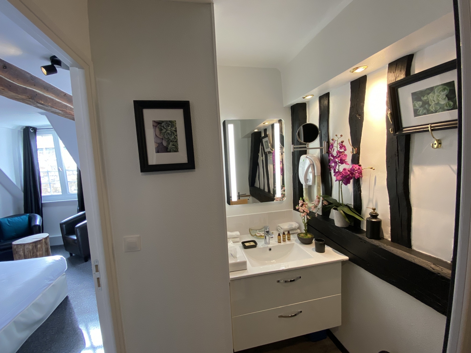 Salle de bain du studio de l’Hôtel de la Cathédrale à Rouen, avec poutres apparentes, meuble vasque moderne et orchidée décorative.