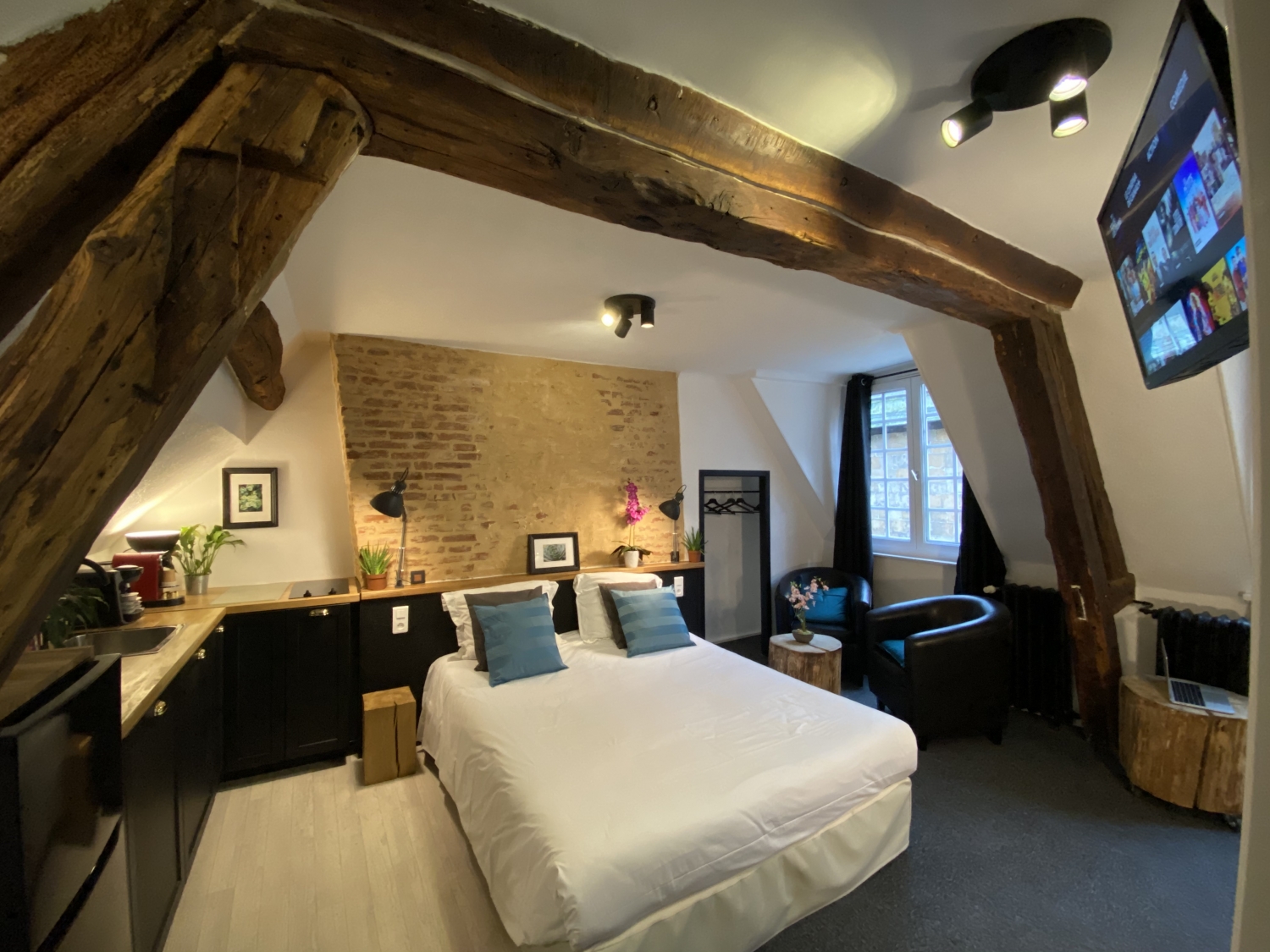 Studio de l’Hôtel de la Cathédrale à Rouen avec poutres apparentes, mur en briques, lit double confortable et coin salon cosy.