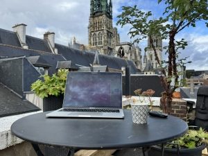 Ordinateur portable sur une table de terrasse avec vue sur la cathédrale de Rouen, ambiance de travail en plein air.
